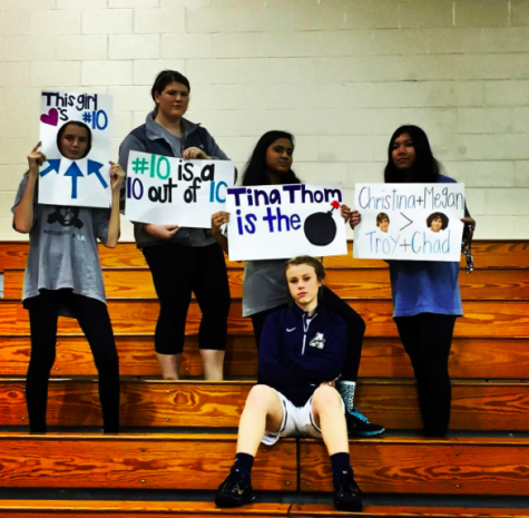 Fans cheer on their friend with posters at an Academy basketball game.
